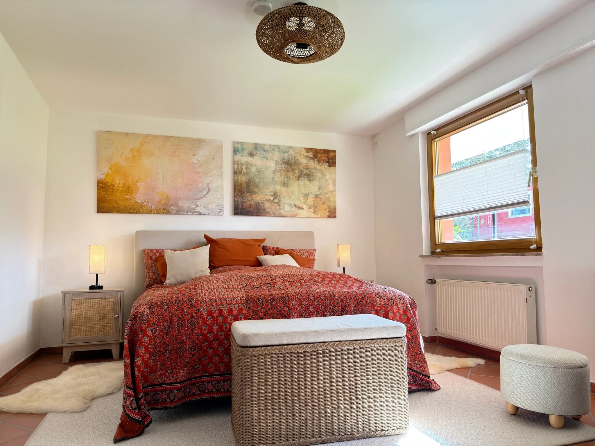 Schlafzimmer mit Boxspringbett, Kunstdrucken, Rattanlampe und Truhe am Fußende.